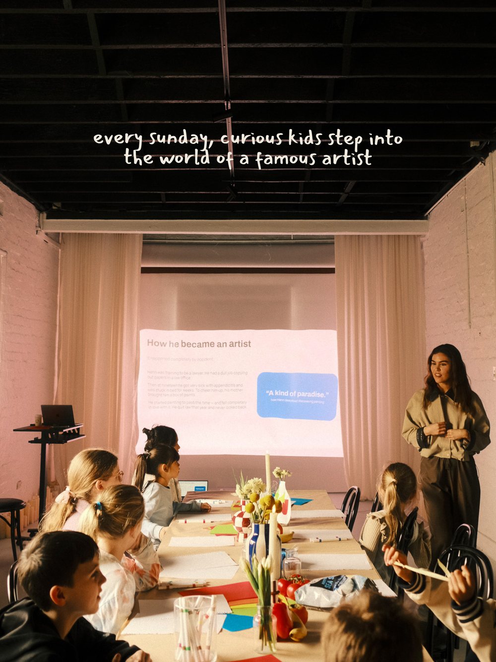Children along the long table as the story of the artist is shown on the screen