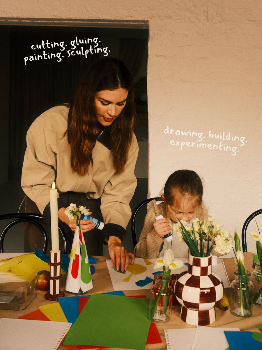 A tutor leaning in beside a child mid-make, cutting and gluing